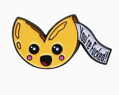 The Sassy Fortune Cookie Enamel Pin by Blue Dog Posters showcases a cartoon-style fortune cookie with a surprised expression and rosy cheeks. A piece of fortune paper emerges, boldly stating "You're Fucked!" in black letters. This humorous pin design is both playful and cheeky, making it a delightful accessory with a mischievous twist.