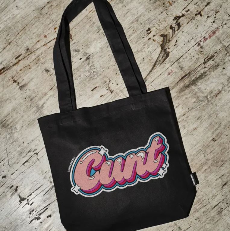The CUNT Tote Bag Black by Blue Dog Posters is a premium cotton canvas bag with “Cunt” in bold, colorful bubble letters on the front, shown on a distressed wooden surface.