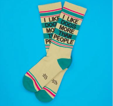 The I Like Dogs More Than People Gym Crew Socks by Blue Dog Posters are beige with green toes, heels, and stripes, and bold black text—an ideal funny gift for dog lovers. Shown on a bright blue background.
