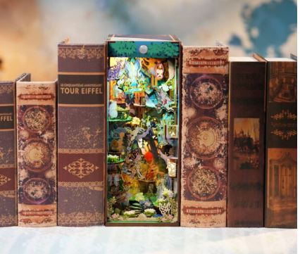 A row of vintage books stands upright; one open book displays the Blue Dog Posters A Midsummer Night's Dream Large Book Nook by Tonecheer, revealing a vibrant 3D forest scene and hidden animals—like a library of secrets.