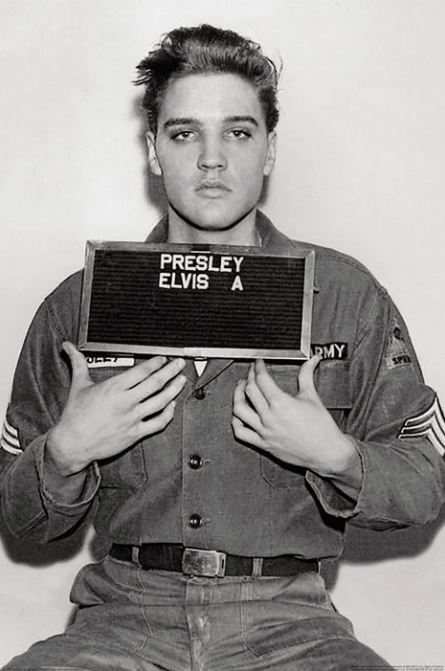 A young man in uniform poses for the MUS 181 "Elvis Presley Mug Shot" black-and-white music poster, holding a sign reading "PRESLEY ELVIS A" against a plain background.