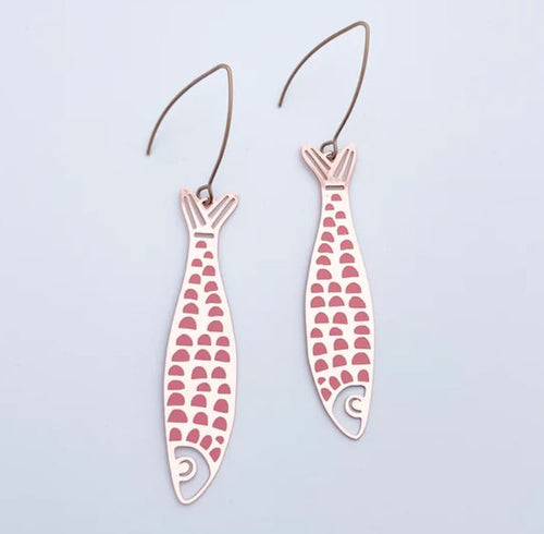The Denz Midi Fishy Rose Gold Pink Earrings from Blue Dog Posters are a pair of lightweight, vertically-oriented earrings shaped like fish. They feature a pink and white scale pattern against a light blue background and are crafted from recycled stainless steel with hooks attached at the top.