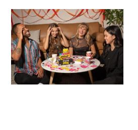 Four people gather around a table playing Match My Freak by Blue Dog Posters, laughing and smiling. Cards and cups fill the table, while colorful streamers in the background create a festive vibe for this adult party game.