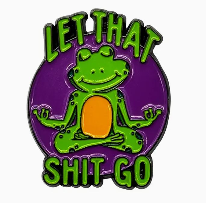 The "Let That Shit Go Frog Enamel Pin" by Blue Dog Posters showcases a meditating cartoon frog in a serene pose with eyes closed. Above and below the frog, bold green text reads "LET THAT SHIT GO." Set against a purple background, this colorful soft enamel pin exudes calm and relaxation.
