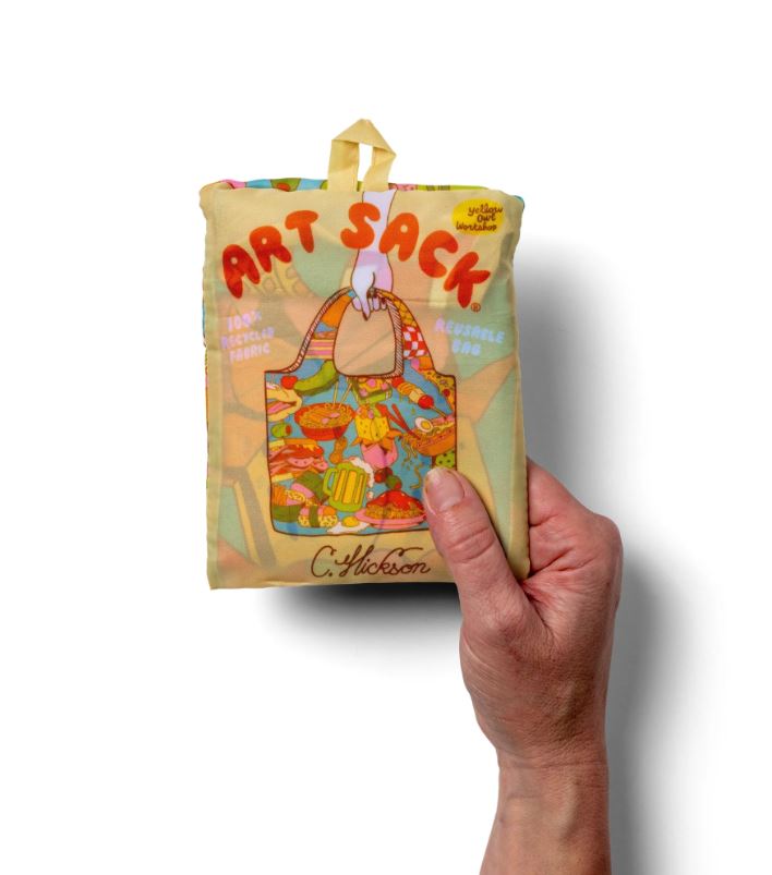A hand holds the Clay Hickson Gourmand Art Sack from Blue Dog Posters, a folded rPET bag with colorful food art, large bag illustration, and packaging labeled “100% Recycled Fabric” and “C. Hickson.”.