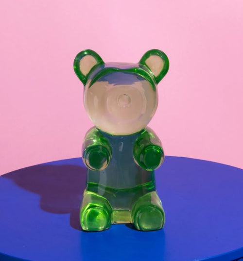 The Barry Bear Green Resin by Blue Dog Posters is a translucent green bear sitting upright like a gummy bear on a bright blue surface, with a pink background—perfect as playful desk decor or a paperweight.
