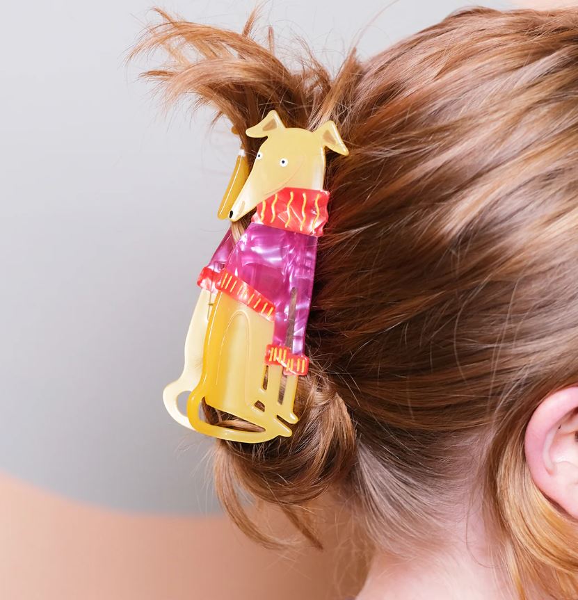 A person with reddish-brown hair secures their updo using the Blue Dog Posters Grey Hound in a Jumper Hair Claw, a whimsical plant-based acetate clip shaped like a dog in a pink and orange scarf and cute jumper.