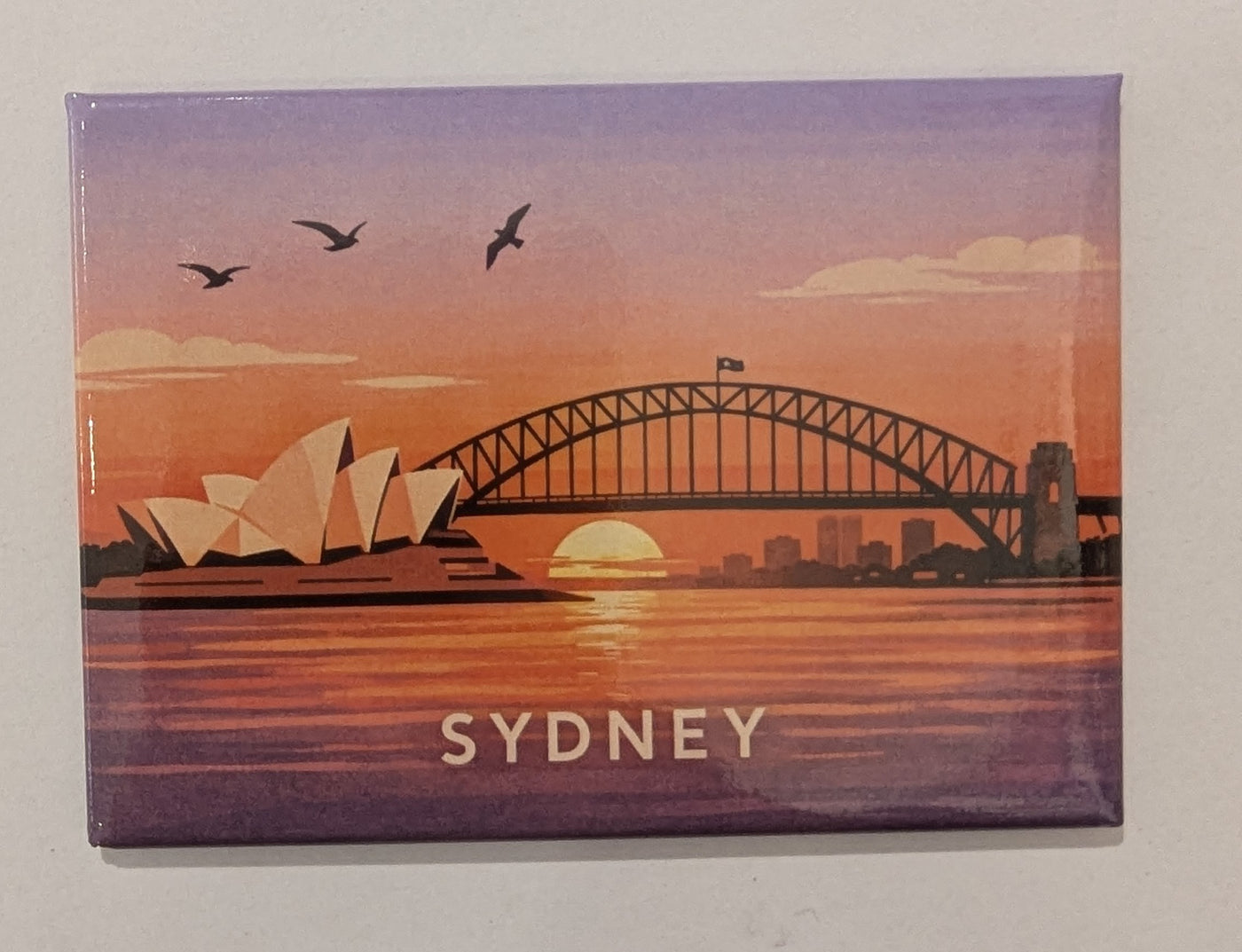 Travel Magnet - Sydney Harbour Sunset by Blue Dog Posters features the Opera House and Harbour Bridge at sunset with birds in flight and "SYDNEY" below—an ideal Australia-themed novelty fridge magnet or travel souvenir.
