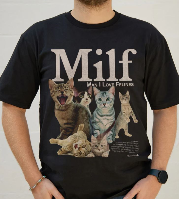 A person wearing a relaxed fit Blue Dog Posters Man I Love Felines T-Shirt Black MED, featuring five cats and bold "Milf" text with "Man I Love Felines" below.