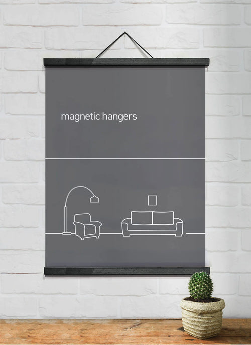 A gray poster with white line art of living room furniture, including a couch, armchair, lamp, and picture frame, hangs from a white brick wall using Blue Dog Posters' Magnetic Timber Hanger 51cm Black Pair. A small cactus in a woven pot sits on a wooden surface below the poster.