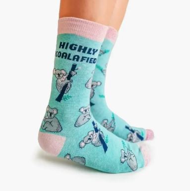 A person wears Blue Dog Posters' Koalafied Socks: light blue women’s socks with pink trim, cartoon koalas, and “HIGHLY KOALAFIED” above a koala holding a eucalyptus branch. Made from soft combed cotton for comfort.