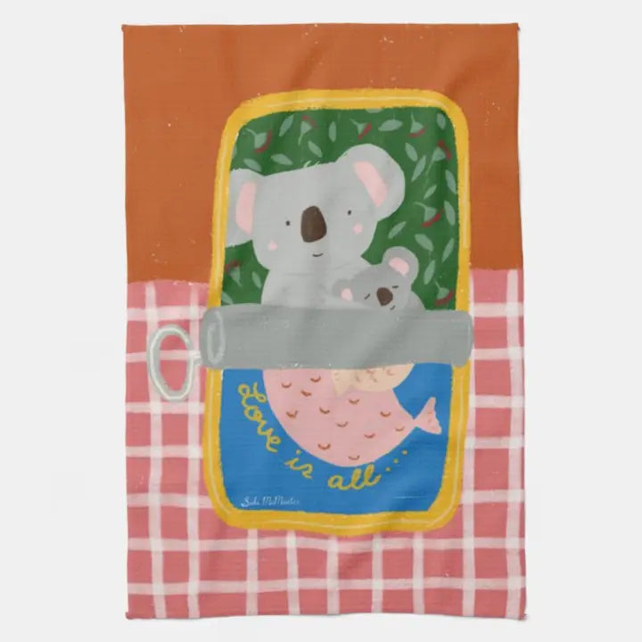 The Koala Sardine Kitchen Tea Towel by Blue Dog Posters features a 100% cotton design of a koala cuddling a baby wrapped in pink, framed by a yellow window and "Love is all..." below. It has a red top and pink checkered bottom—perfect for your kitchen.