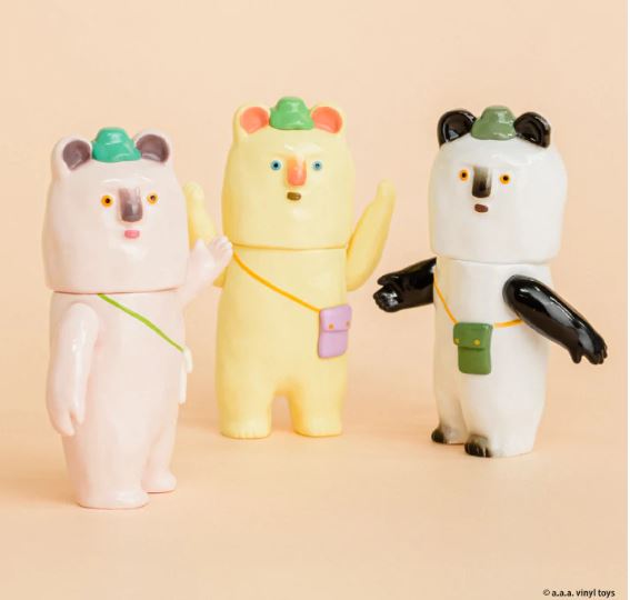 Three pastel pink, yellow, and white bear-shaped Kurikun Figure Blind Box minis by Blue Dog Posters, each with a small hat and crossbody bag like Staaan, stand side by side with one arm raised against a beige background.