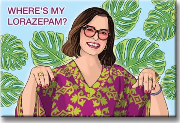 A smiling woman with short brown hair and glasses wears a purple-green patterned top, standing before lush leaves. The Blue Dog Posters "Wheres my Lorazepam Victoria Magnet" displays the quote, “WHERE’S MY LORAZEPAM?,” made in the USA.