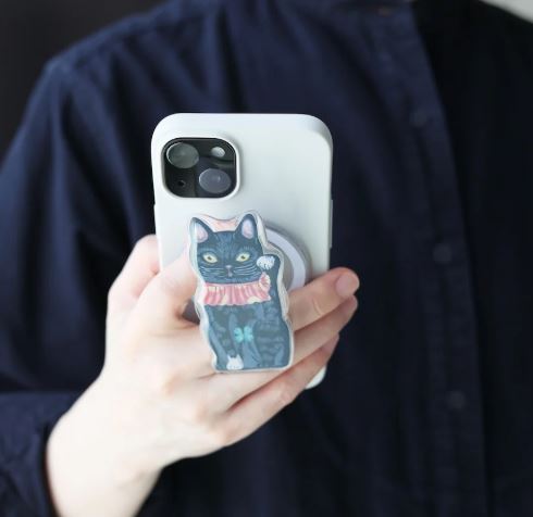 A person in a dark shirt holds a white smartphone with the Blue Dog Posters Magnetic Phone Grip Cats - Lucky Cat Black attached.