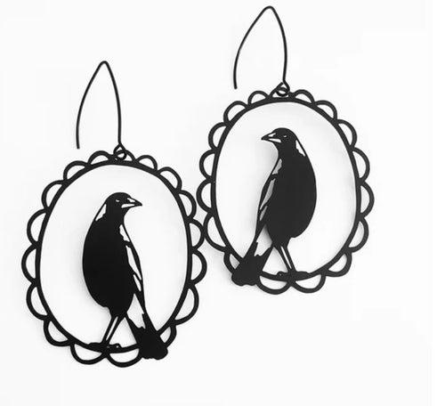 Magpie Black Earrings by Blue Dog Posters feature bird silhouette cutouts within scalloped oval frames on a white background. They are crafted from lightweight recycled stainless steel and have surgical steel hooks for added comfort.