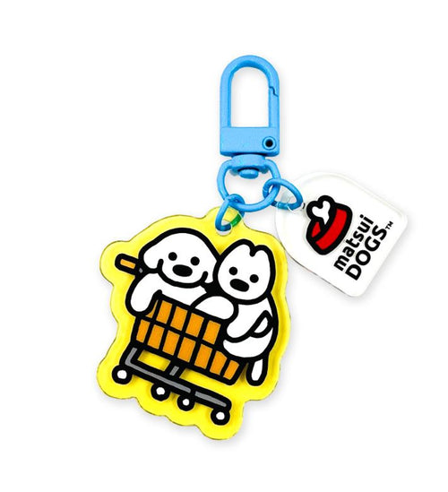 The Matsui Dogs Japanese Acrylic Keyring by Blue Dog Posters features two cartoon dogs in a yellow cart, a blue clip, a white "matsui DOGS" tag, and a red and white cartoon hat.