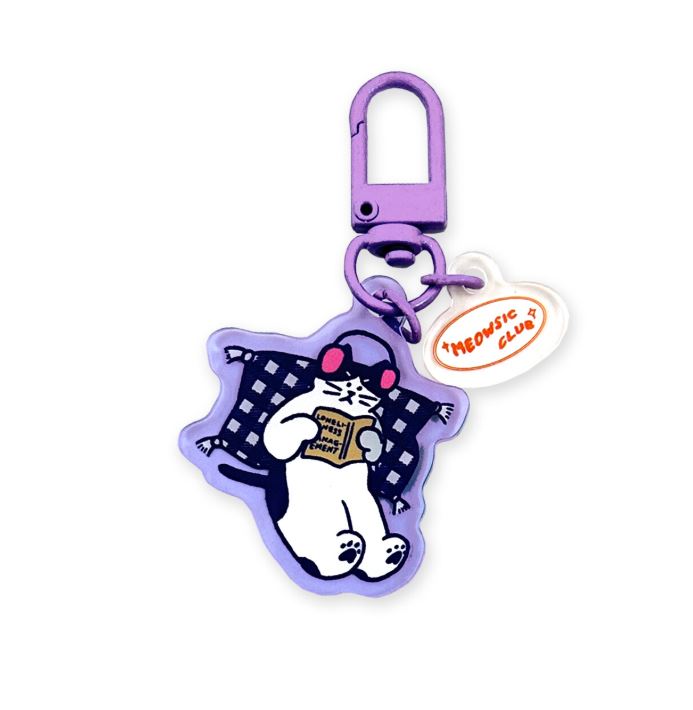 The Meowsic Club Cat Japanese Acrylic Keyring by Blue Dog Posters is a purple Japanese acrylic keyring featuring a cartoon cat with pink headphones on a checkered pillow reading, plus a white “Meowsic Club” tag in orange.