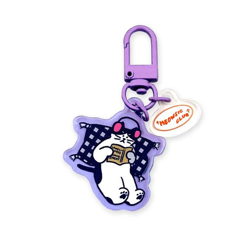 The Meowsic Club Cat Japanese Acrylic Keyring by Blue Dog Posters is a purple Japanese acrylic keyring featuring a cartoon cat with pink headphones on a checkered pillow reading, plus a white “Meowsic Club” tag in orange.