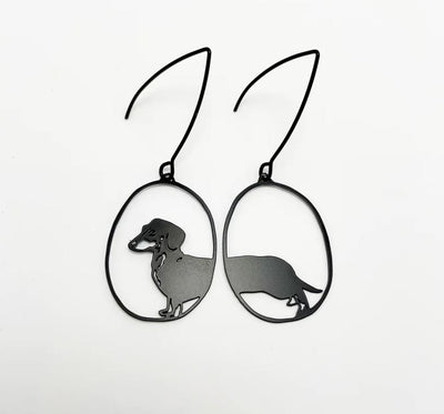 Introducing the "Mini Dachshund Earrings" by Blue Dog Posters—these lightweight earrings are crafted from recycled stainless steel and display a dachshund silhouette within oval-shaped frames, set against a minimalist white background.