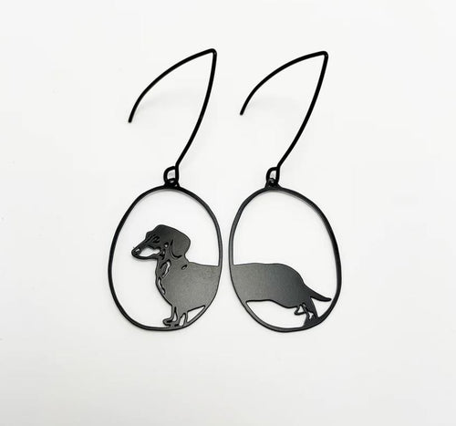 Introducing the "Mini Dachshund Earrings" by Blue Dog Posters—these lightweight earrings are crafted from recycled stainless steel and display a dachshund silhouette within oval-shaped frames, set against a minimalist white background.