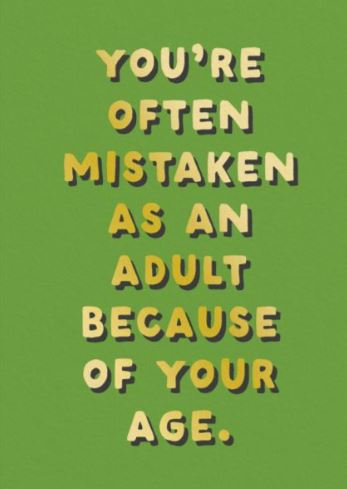Text on a green background reads: "You're often mistaken as an adult because of your age," in uppercase with highlighted letters and brown shadows, printed on a gold foil Mistaken As an Adult Greeting Card by Blue Dog Posters.