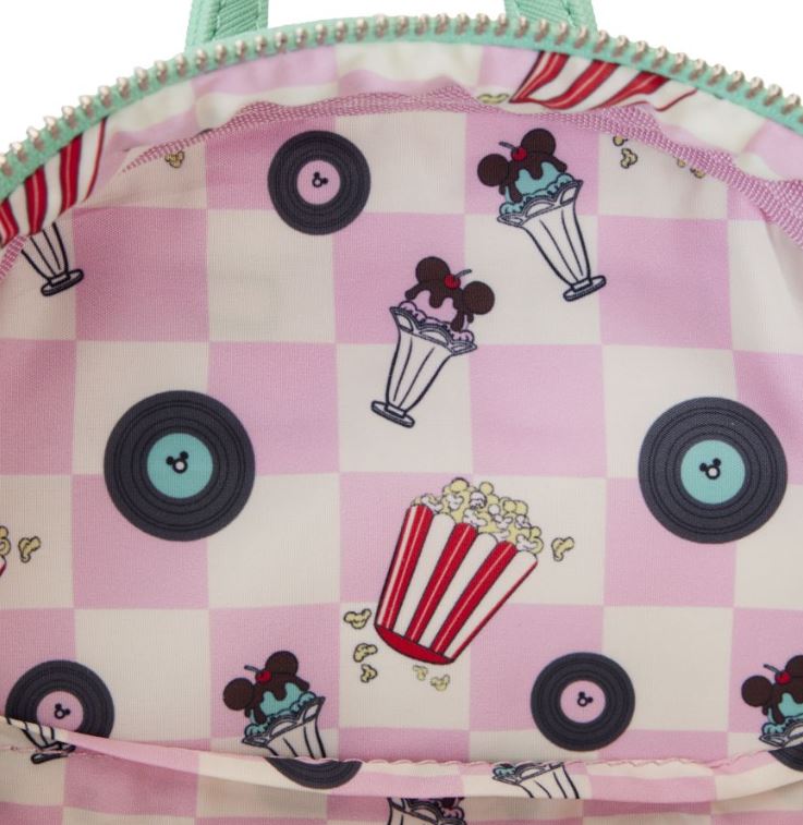 A close-up image of an open Disney Mickey & Minnie Date Drive In Backpack by Blue Dog Posters, showcasing a pastel pink and white checkered interior adorned with designs of ice cream sundaes with mouse ears, vinyl records, and popcorn buckets scattered throughout. The zipper and straps are light green.