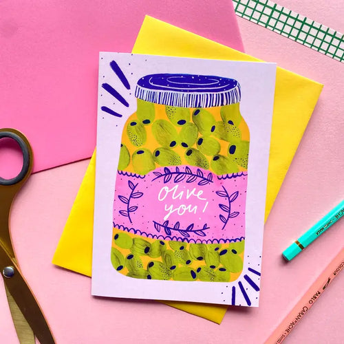 The Olive You Greeting Card by Blue Dog Posters features a colorful illustration of a green olive jar with a pink "Olive you!" label, set against vibrant backgrounds—perfect for sharing cheerful greetings.