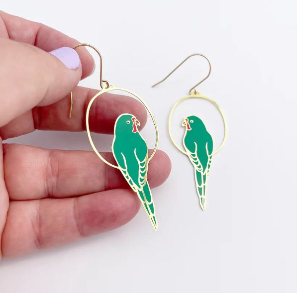 A hand holds a Blue Dog Posters Parrot in Green Denz Earring shaped like a green parrot in a hoop, with its lightweight matching earring beside it on a white background.