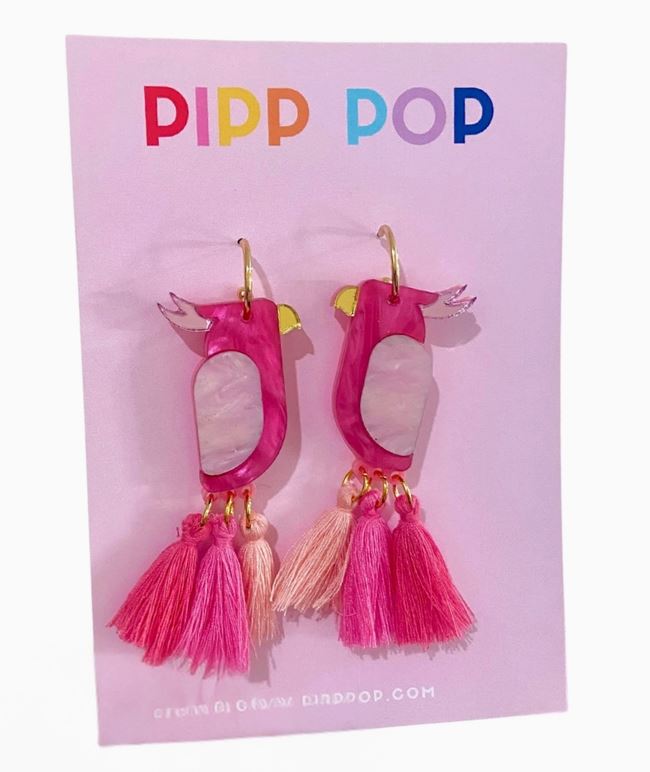A pair of Pink Galah Dangles by Blue Dog Posters, featuring pink and white colors with tassels, shown on a pastel purple card.