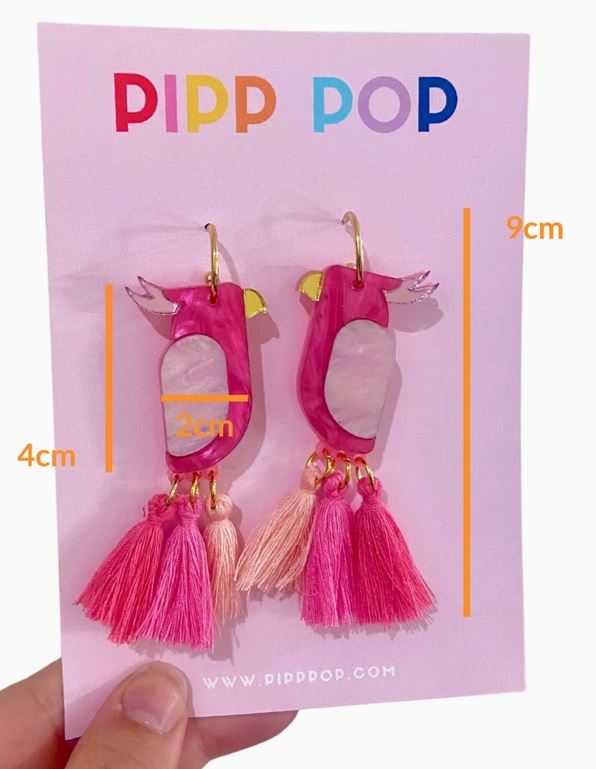 The Pink Galah Dangles by Blue Dog Posters are parrot-shaped earrings with gold hooks and pink tassels, inspired by Australian birds. Each earring is about 4cm x 2cm and comes on a 9cm tall "PIPP POP" display card.