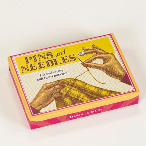 The Blue Dog Posters Pins and Needles Small Tin features vintage sewing art, the phrases “PINS and NEEDLES,” “I like when my shit turns out cool,” and “I’M ON A JOURNEY.” Ideal for crafting or organizing supplies.
