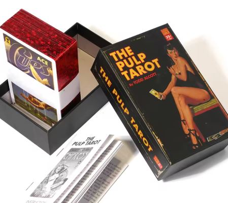 The Pulp Tarot Cards by Blue Dog Posters feature vintage pulp magazine art on the box, with a woman illustrated, a black booklet, and tarot cards partially in a red case showing the Ace of Cups.