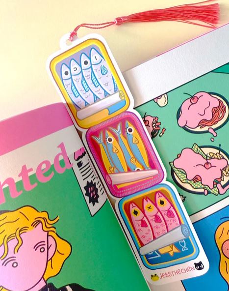 The Bookmark Sardine Stack by Blue Dog Posters shows four tinned fish cans stacked vertically with illustrations. It features a pink tassel and includes the artist's name, Jess Chen, at the bottom.