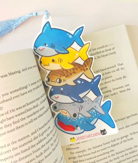 The Bookmark Shark Stack from Blue Dog Posters features six cute cartoon sharks and a blue tassel, bringing fun marine vibes to your stationery. It includes a small "Jestthechen" logo at the bottom.