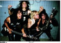 Four rock musicians with long hair and guitars pose in front of a blue tiled wall, shouting together in dark outfits. The MUS 029 Slayer 1986 poster is perfect to add an edgy rock vibe to your music collection.