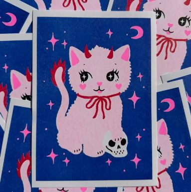 The Spooky Cat A5 Risograph by Amy Hastings for Blue Dog Posters features a pink cartoon cat with red accents on a blue background with stars and moons, printed on recycled coffee cup paper for a playful risograph effect.