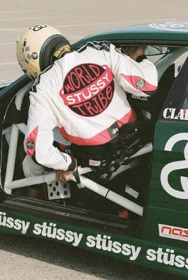 A race car driver in racing gear climbs into a car with "stüssy" on the side. The Stussy Motorsports poster by ALT 059 showcases vibrant detail, printed on premium 150gsm gloss paper.