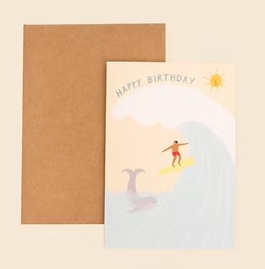 The Surfer Birthday Card by Blue Dog Posters features a surfer riding a wave with a dolphin below, a smiling sun above, and "Happy Birthday" at the top. Includes a brown envelope.