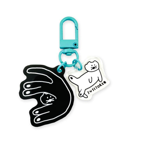 The Susstore Cats Japanese Acrylic Keyring by Blue Dog Posters features two charms—a black hand holding a white cat and a cartoon cat with "JUSTOKED"—plus teal blue hardware, making it an ideal bag accessory.