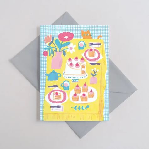 The Tea Party Greeting Card by Blue Dog Posters features a cheerful tea party scene with cakes, a teapot, flowers, and an orange cat on a checkered tablecloth. This A6 card is plastic free and comes with a gray envelope.