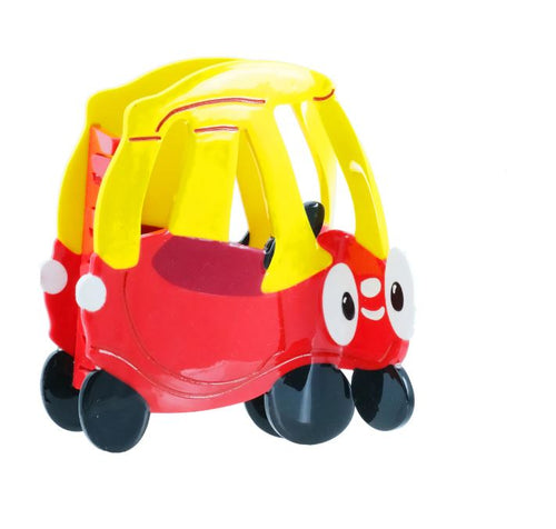 The Blue Dog Posters Tiny Tike Car Hair Claw features a small red and yellow car with cartoon eyes, a smiling face, black wheels, and an open top—nostalgic hair accessory photographed on a white background.