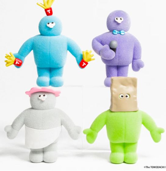 Four vibrant plush toys from the Tomodachi Figure Vol 3 Blind Box by Blue Dog Posters are shown: a blue one with red "T" gloves, a purple with bow tie and mic, a gray in pink hat and skirt, and a green with paper bag over its head.