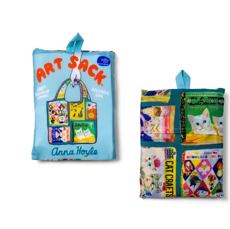 Two reusable Useless Books Art Sack bags by Blue Dog Posters are shown. The front shows colorful cats, books, and “Art Sack” with “Anna Hoyle”; the back features vintage book covers and cat art. Both have blue handles.