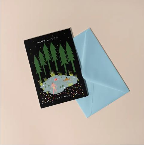 The Blue Dog Posters Stay Wild Swimming Birthday Card features wild swimmers in a pine-fringed pond, with "Happy Birthday" and "Stay Wild" text, plus a light blue envelope—ideal for adventure lovers.