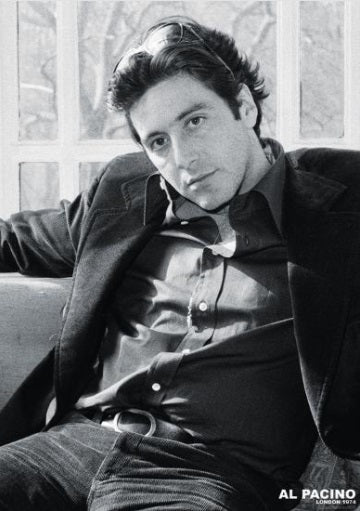 Black and white image of a man with dark hair reclining on a seat, wearing a dark button-up shirt, jeans, and jacket. He has a contemplative look and is in front of a window. "AL PACINO" is written in small white text at the bottom right corner. This Al Pacino - London 1974 poster by MTV 266 is a true Film Classic for any Movies & TV Collection.