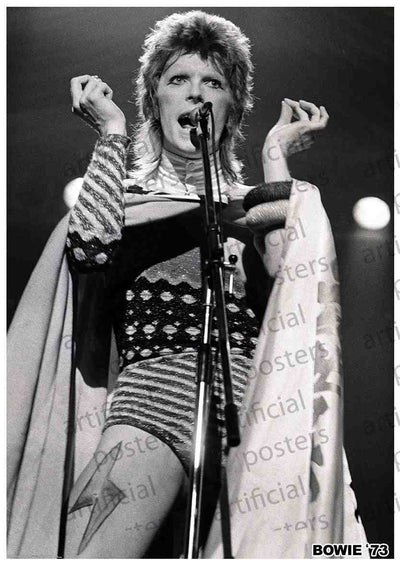 Black and white image of a performer on stage in 1973. The performer, David Bowie as Ziggy Stardust, is singing into a microphone, dressed in a flamboyant outfit with striped patterns and a cape. This MUS 013 image has a watermark reading "artificial" and is labeled "BOWIE '73" in the bottom right corner, perfect for any music collection.