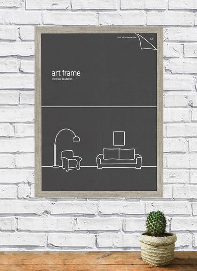A Classic Frame 60x80cm Ash from Blue Dog Posters, featuring minimalist furniture line drawings in black and white, hangs on a white brick wall, encased in sleek plexiglass. Below on a wooden surface rests a small cactus in a pot.