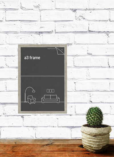 A framed poster from Blue Dog Posters hangs on a white brick wall, showcasing the text "Classic Frames Collection" along with minimalist furniture illustrations. Below, a small potted cactus rests on a wooden table. The scene exudes a clean and modern aesthetic with its Classic Frame A3 Ash.
