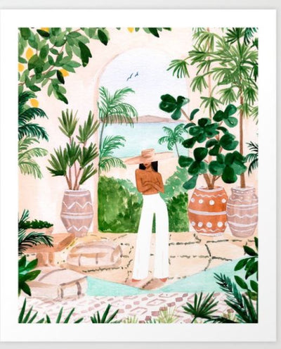 The GAL42 Art Print "Peaceful Morocco II" by Sabina Fenn features a person in a brown top, white pants, and a wide-brimmed hat amidst lush garden greenery and potted plants. Two birds soar against a light blue sky, beautifully capturing nature's essence.